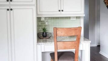 A kitchen with white cabinetry, a wooden chair, and a green backsplash.