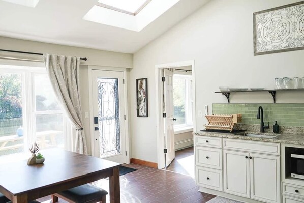 A kitchen with a dining area, a skylight, a door with a decorative glass panel, and a green tiled backsplash.