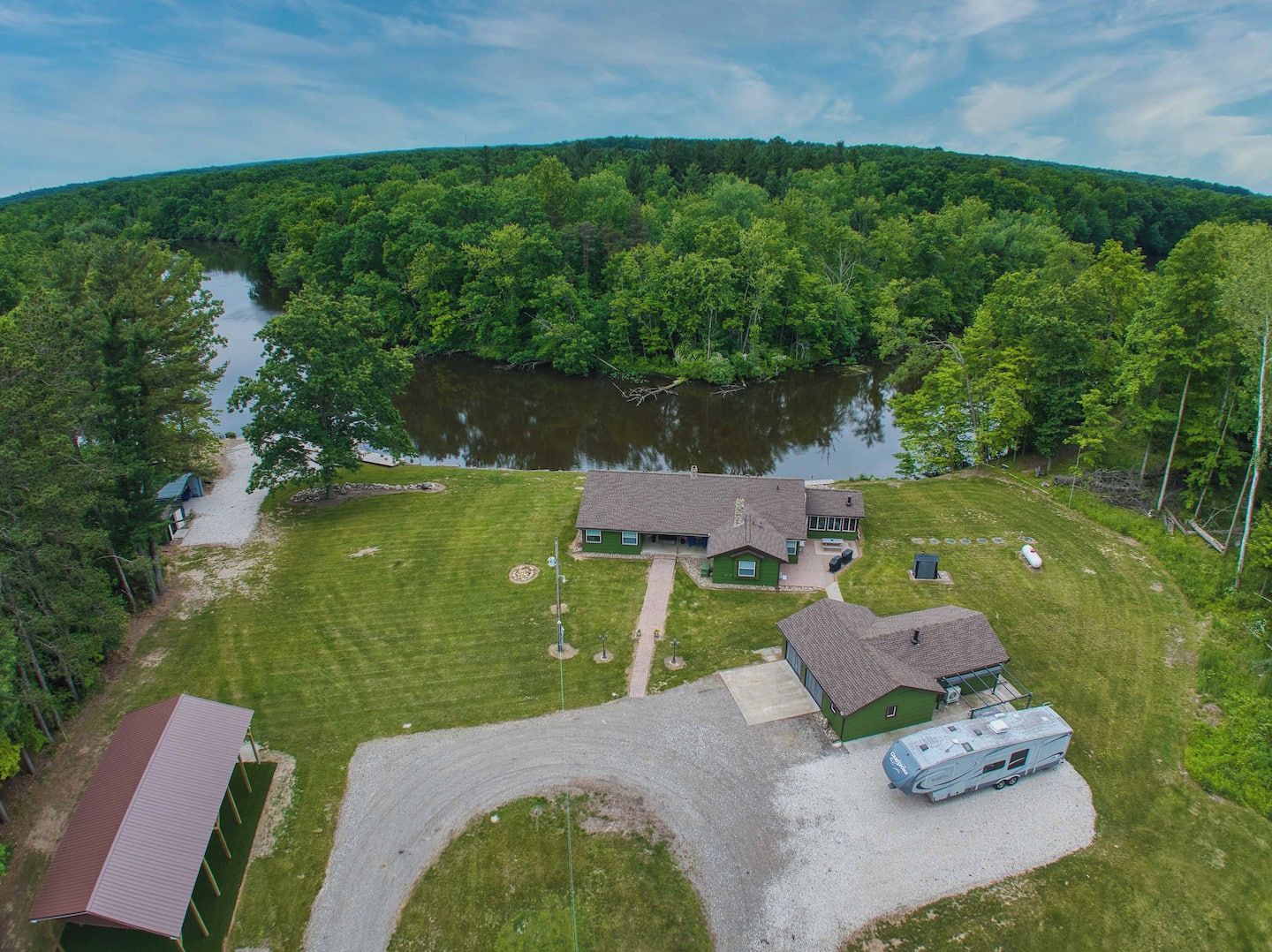 A two-story house with a green roof, a driveway, and a lake in the background.
