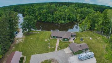 A two-story house with a green roof, a driveway, and a lake in the background.