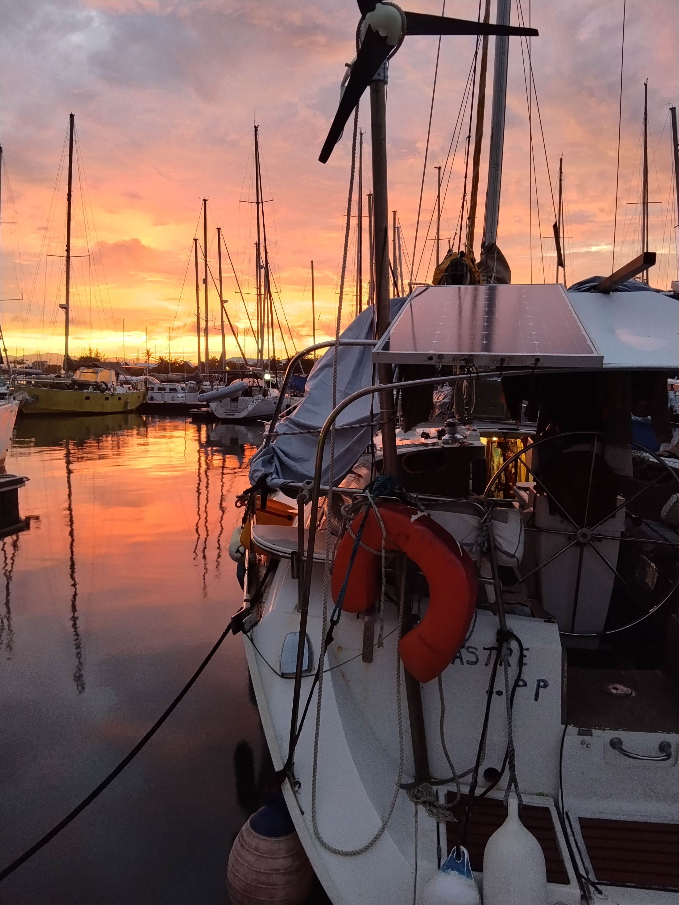 Ein Yachthafen mit mehreren vertäuten Booten, einem Rettungsring und einem Solarpanel auf einem Boot.