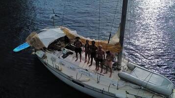 Un velero con un grupo de personas en la cubierta, anclado cerca de una costa rocosa.