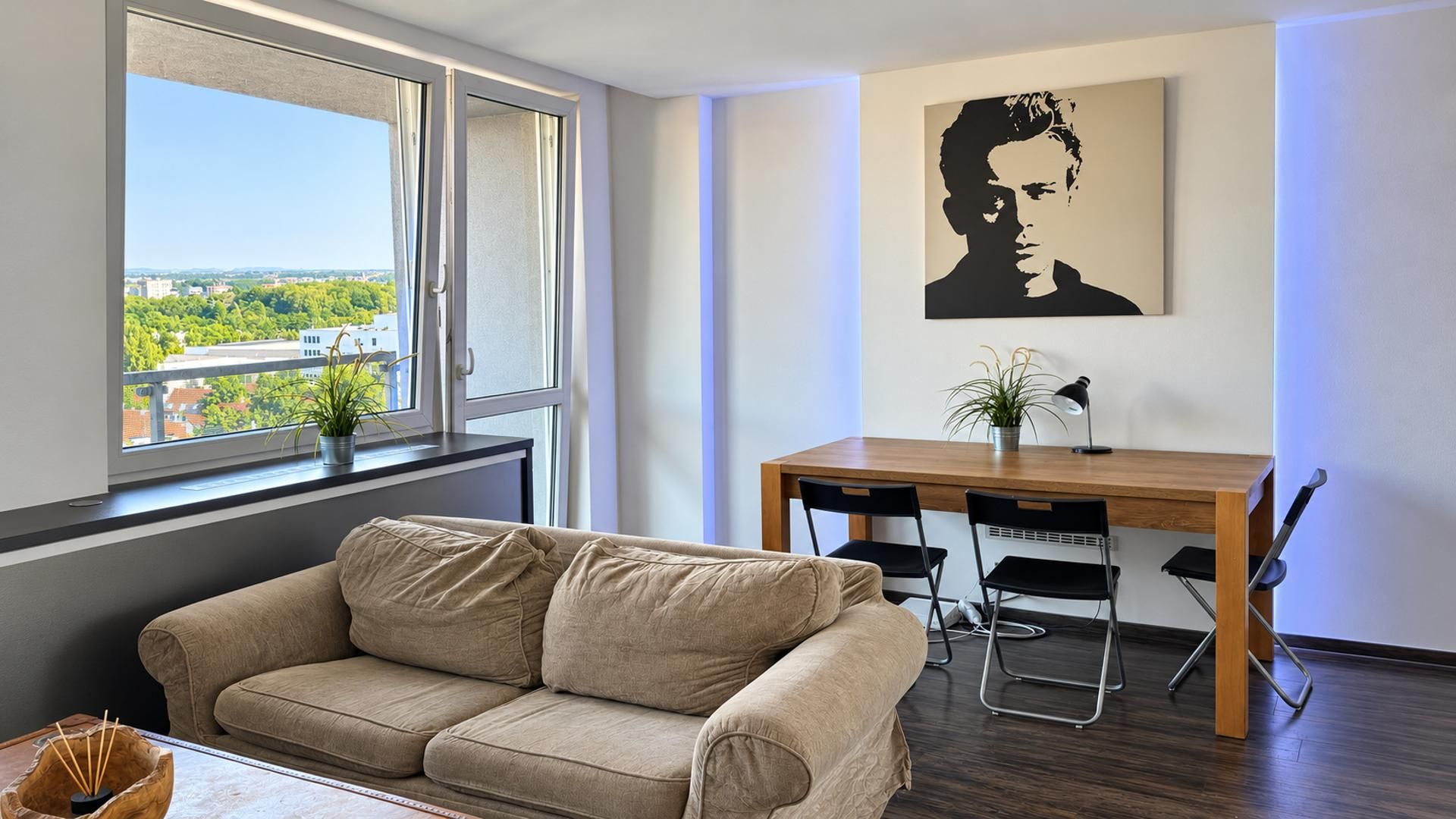 A modern living room with a sofa, a dining table with chairs, a potted plant, and a painting on the wall.