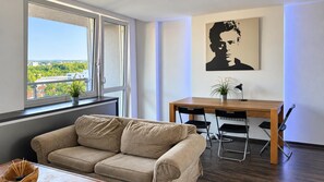A modern living room with a sofa, a dining table with chairs, a potted plant, and a painting on the wall. - 1-bedroom Apartment in Praha 3, Sleeps 2 (Prague)