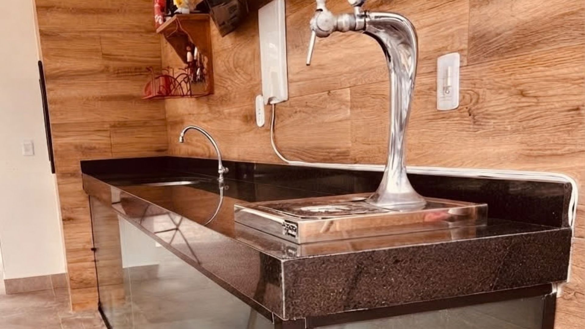 A modern kitchen with a stainless steel sink, wooden backsplash, and a glass countertop.