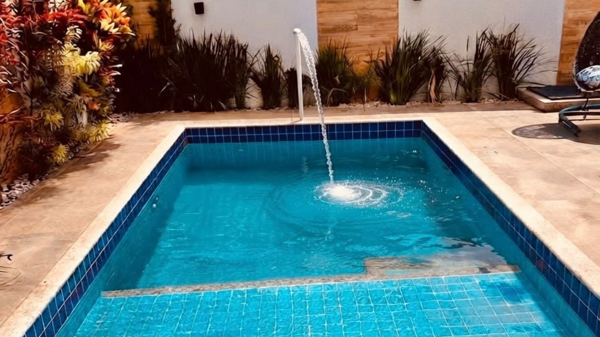 A rectangular swimming pool with a blue tiled interior and a water fountain feature.