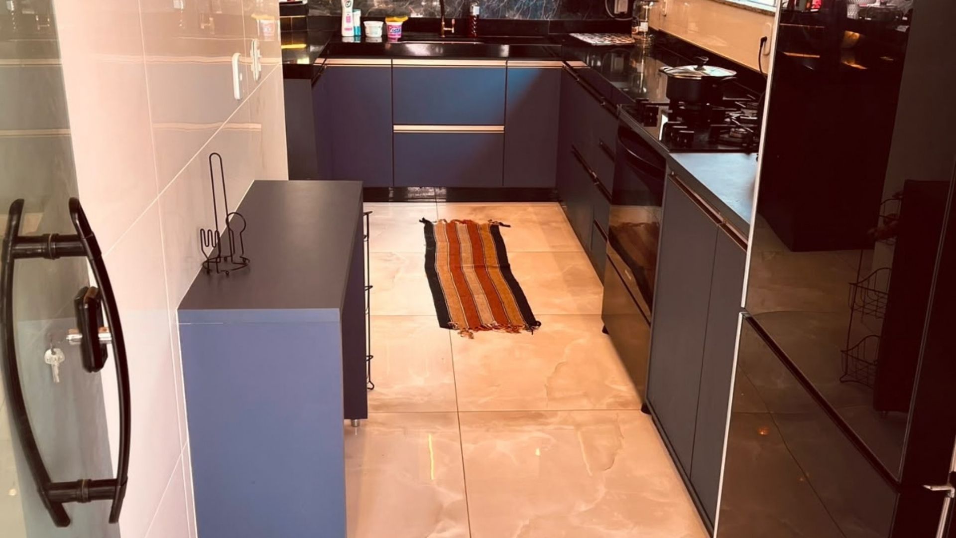 Una cocina moderna con una isla central, armarios azul oscuro y una alfombra a rayas en el suelo.