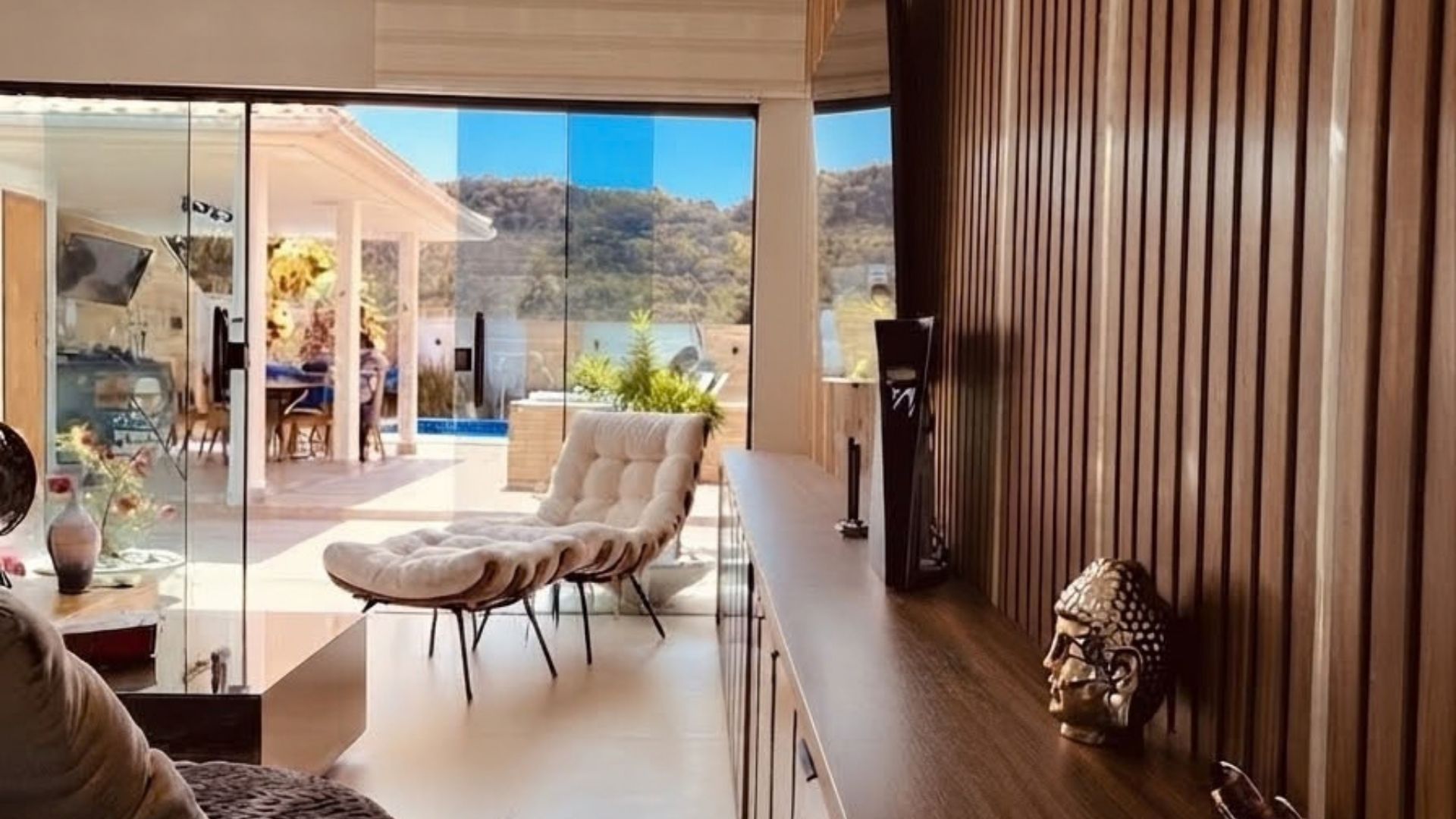A modern interior with a glass wall, a cushioned chair, a wooden table, and a decorative item.