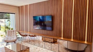 Una sala moderna con un televisor de pantalla plana montado en una pared de madera, una mesa de centro de vidrio y un sillón con cojines.