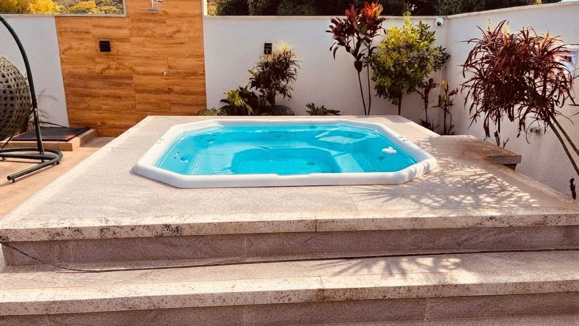 Ein Whirlpool mit Steinrand, umgeben von Pflanzen und einer Holzwand.