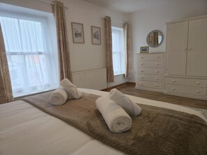 A hotel room with a bed, two rolled towels, a dresser, a mirror, and two framed pictures on the wall. - Garth Pier house with Stunning Views - Pass the Keys (Bangor)