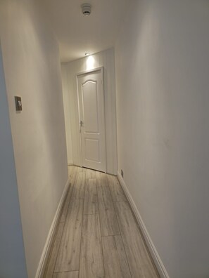 A narrow hallway with a wooden floor and a white door at the end. - 1 Bedroom + Sofa bed in centre of Trearddur Bay - Pass the Keys (Bae Trearddur)