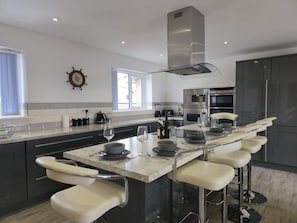 A modern kitchen with a central island, bar stools, a built-in oven, and a large window. - Modern Property with Stunning Mountain views - Pass the Keys (Brynteg)