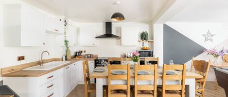 A modern kitchen with white cabinetry, a central island, wooden chairs, and a dining table set for six.