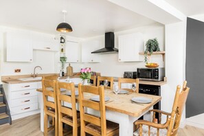 A modern kitchen with white cabinetry, a wooden dining table set for four, and a black range hood. - Two Neighbouring Houses in Cotswolds-Sleeps 18 - Pass the Keys (Stroud)