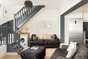 A modern living room with a staircase, a washing machine, a sofa set, and a refrigerator. - Two Neighbouring Houses in Cotswolds-Sleeps 18 - Pass the Keys (Stroud)