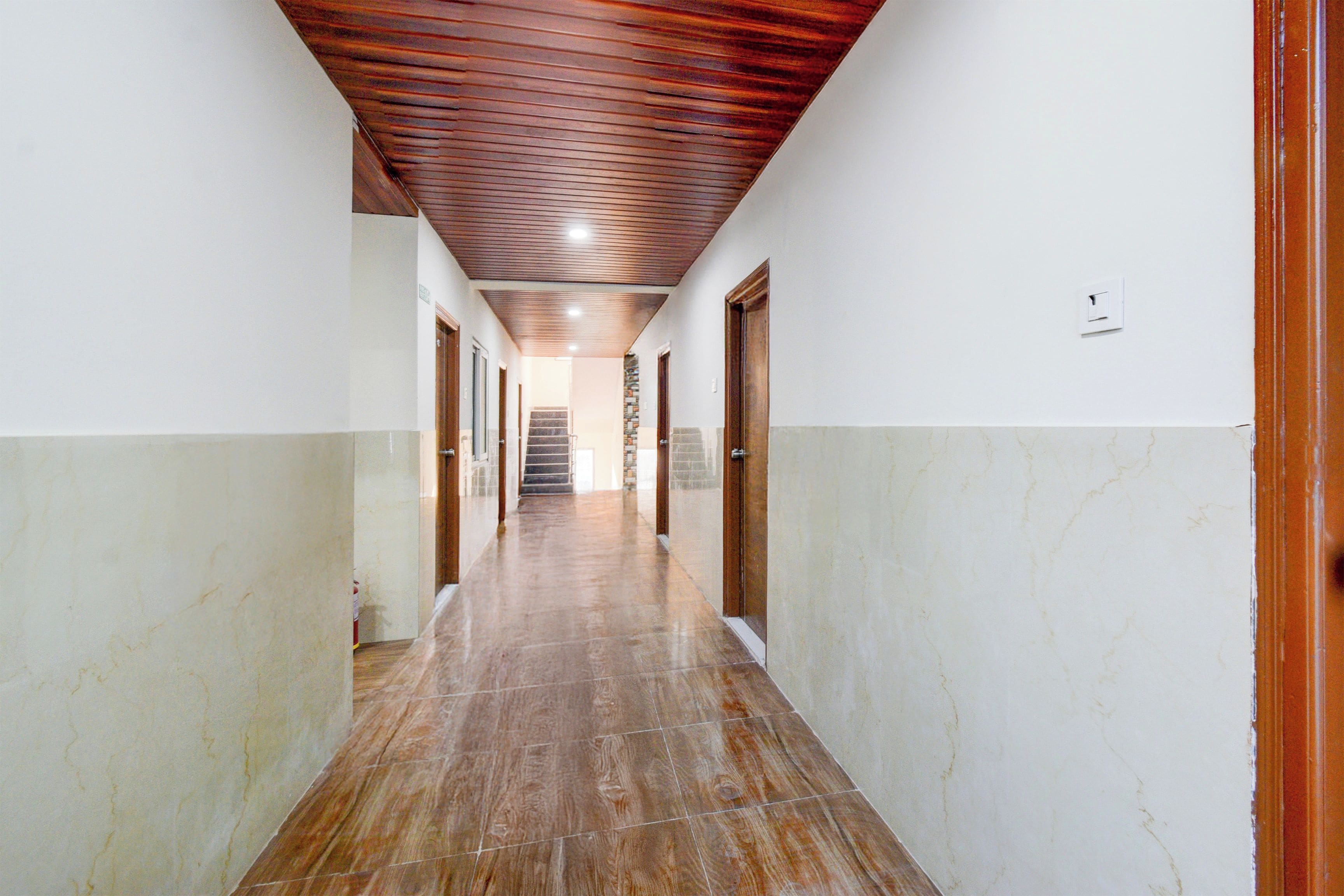 Um corredor com teto de madeira, paredes brancas e chão de mármore que leva a uma escadaria.