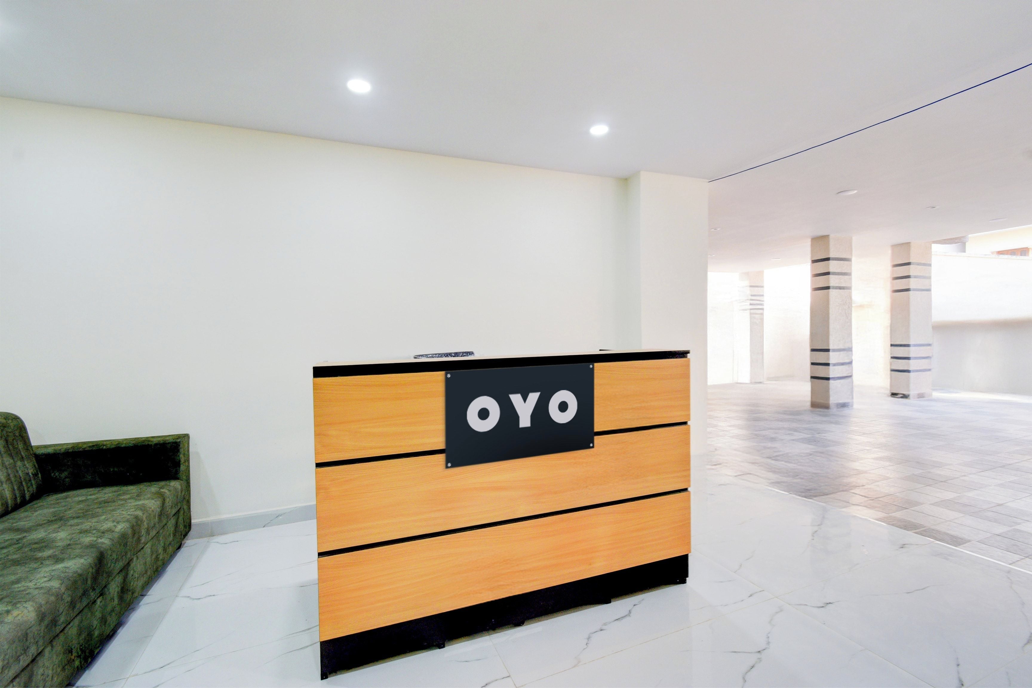 A reception desk with a sign that reads 'OYO' in a modern lobby with marble flooring and a green sofa.