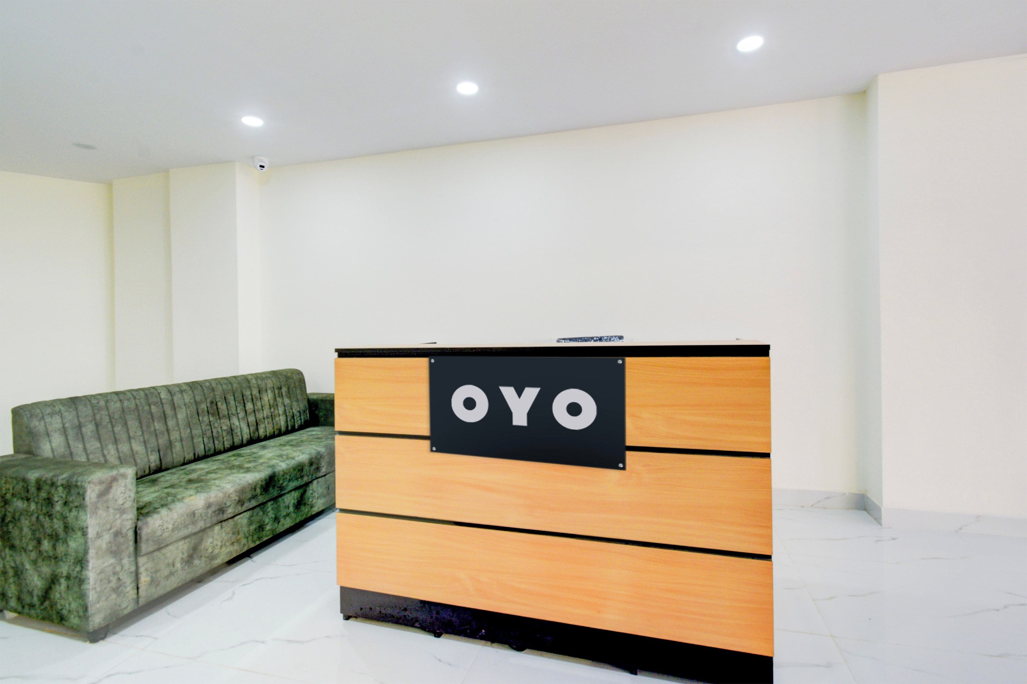 Un mostrador de recepción con un letrero que dice 'OYO' en el vestíbulo de un hotel, con un sofá verde y paredes blancas.
