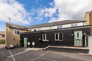 A two-story building with a green door and windows, a parking area, and a clear sky. - Stylish 5-Bed Cotswolds Home|Sleeps 10|Pool table - Pass the Keys (Stroud)
