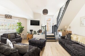 A modern living room with a staircase leading to a second floor, a flat-screen TV mounted on the wall, and a large potted plant. - Stylish 5-Bed Cotswolds Home|Sleeps 10|Pool table - Pass the Keys (Stroud)