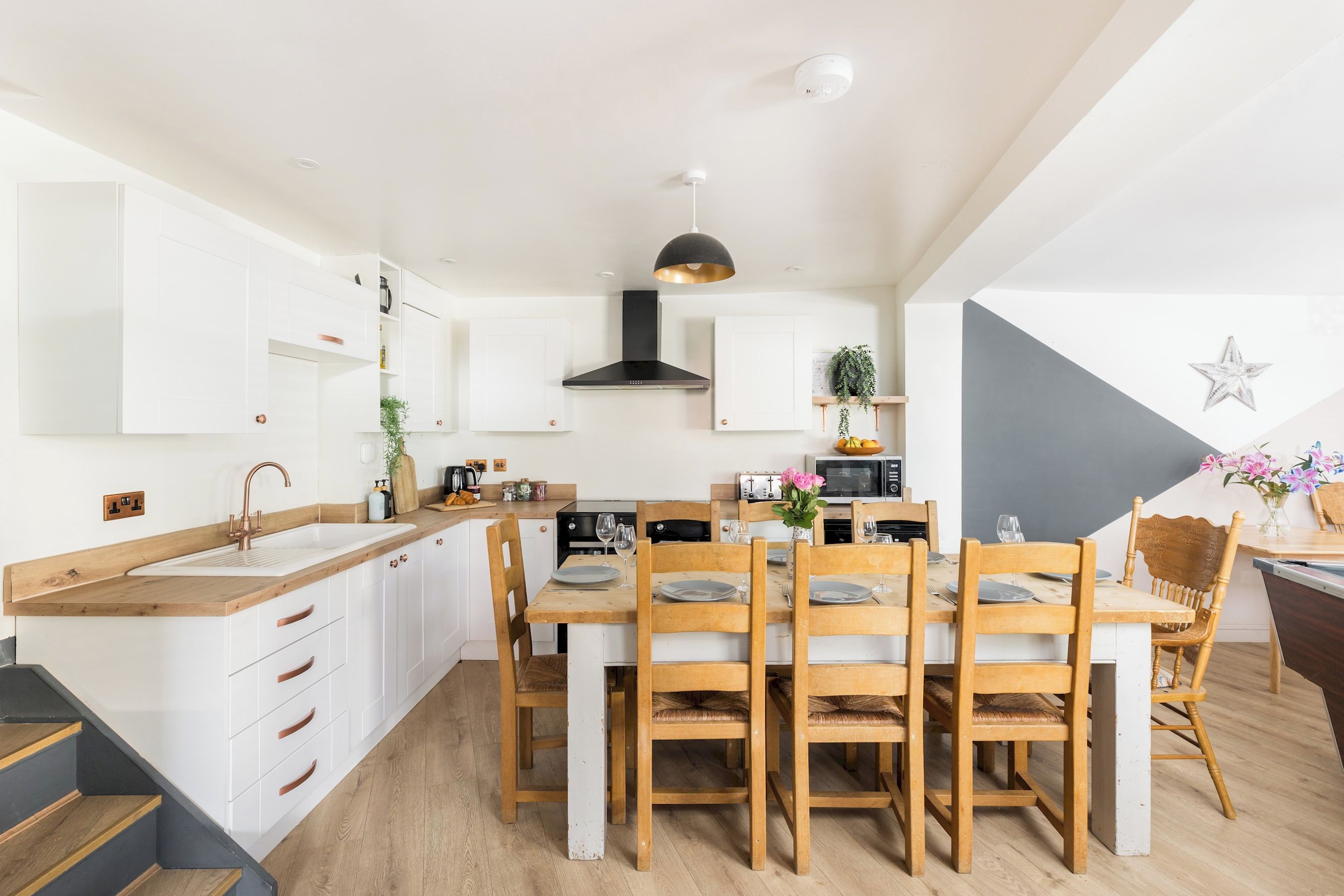 Une cuisine moderne avec des meubles blancs, un îlot central, des chaises en bois et une table à manger pour six personnes.