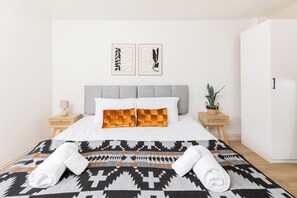 Una habitación de hotel con una cama, dos mesitas de noche, una planta en maceta y dos cuadros en la pared.