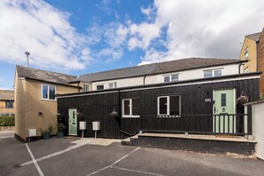 A two-story building with a green door and windows, a parking area, and a clear sky. - Modern 4-Bed Stroud|Sleeps 8|Table Football - Pass the Keys (Stroud)
