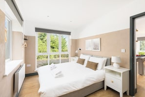 A modern bedroom with a large bed, bedside tables, a lamp, and a view of greenery outside. - Stunning Stroud Retreat: House & Lodge + Gym - Pass the Keys (Stroud)