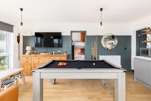 Ein moderner Wohnbereich mit Billardtisch, Fernseher und Küchenzeile.
