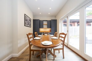 A dining area with a round table, six chairs, and a kitchen in the background. - Spacious 5 Bedroom House with parking and garden - Pass the Keys (Kingston-upon-Thames)