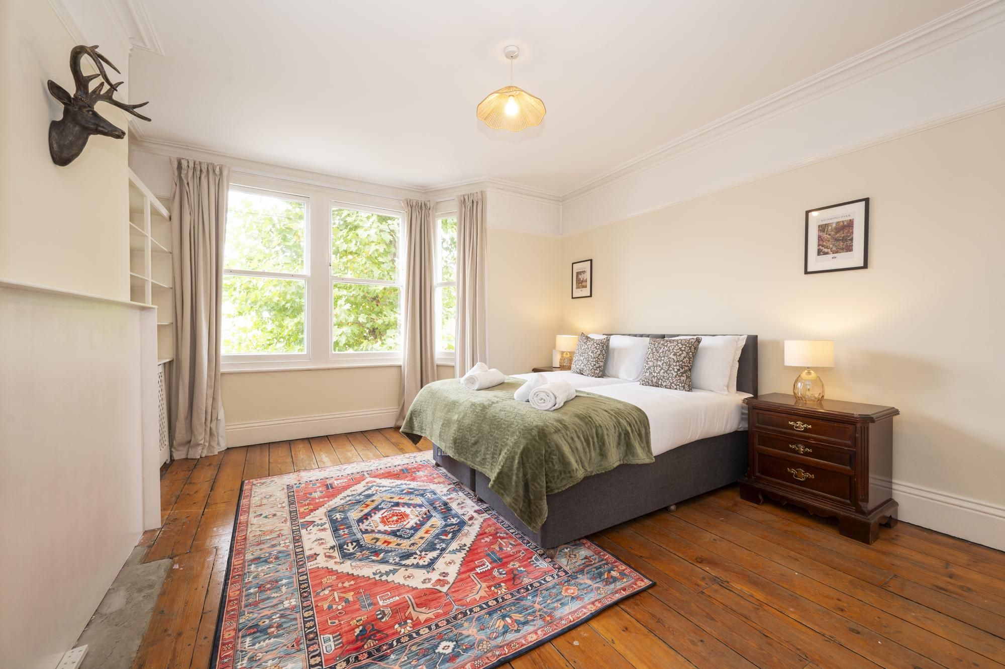 A hotel room with a bed, bedside table, lamp, and a large window with curtains.