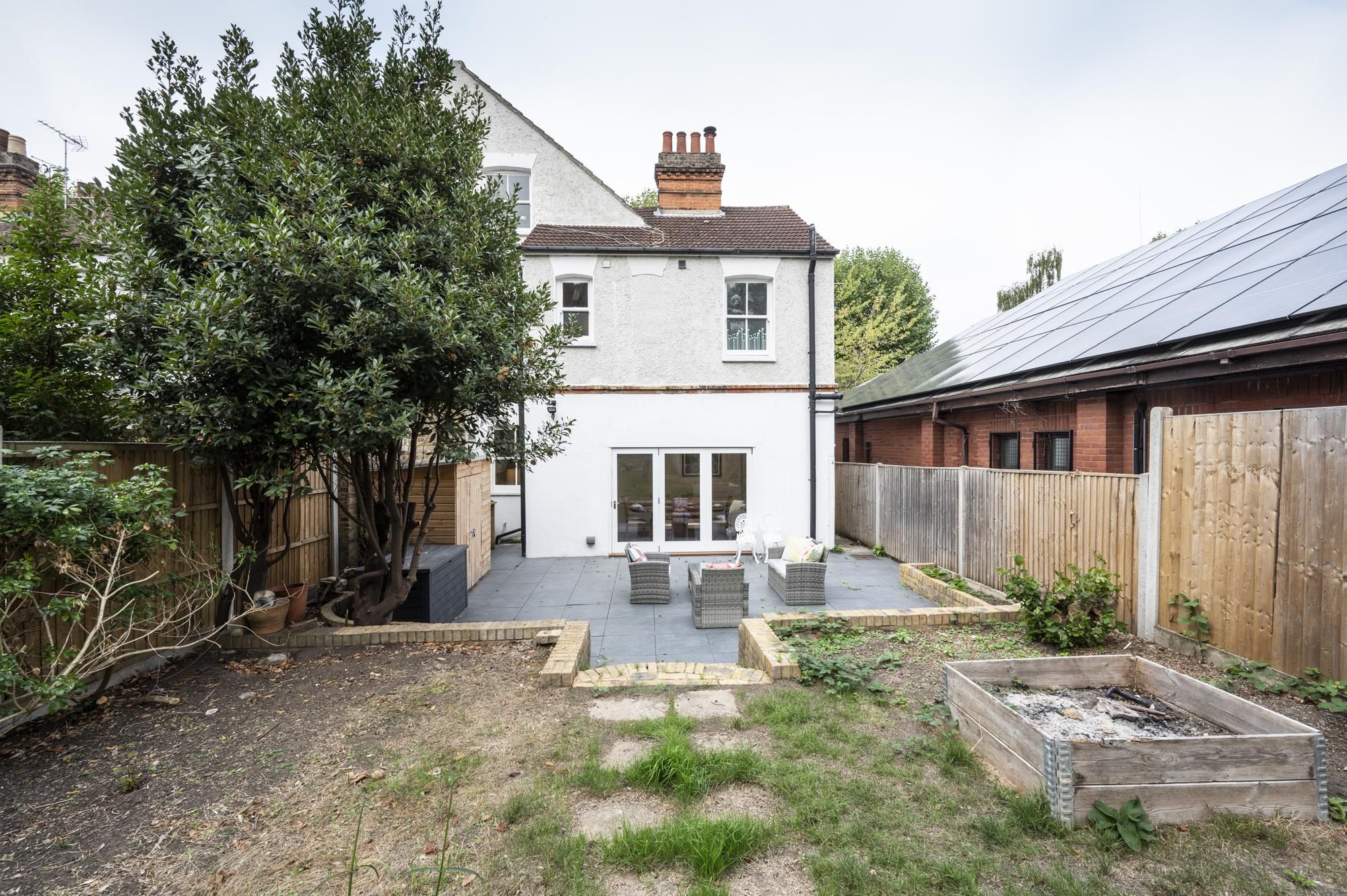 A two-story house with a white exterior, a brick chimney, and a fenced backyard with outdoor furniture.