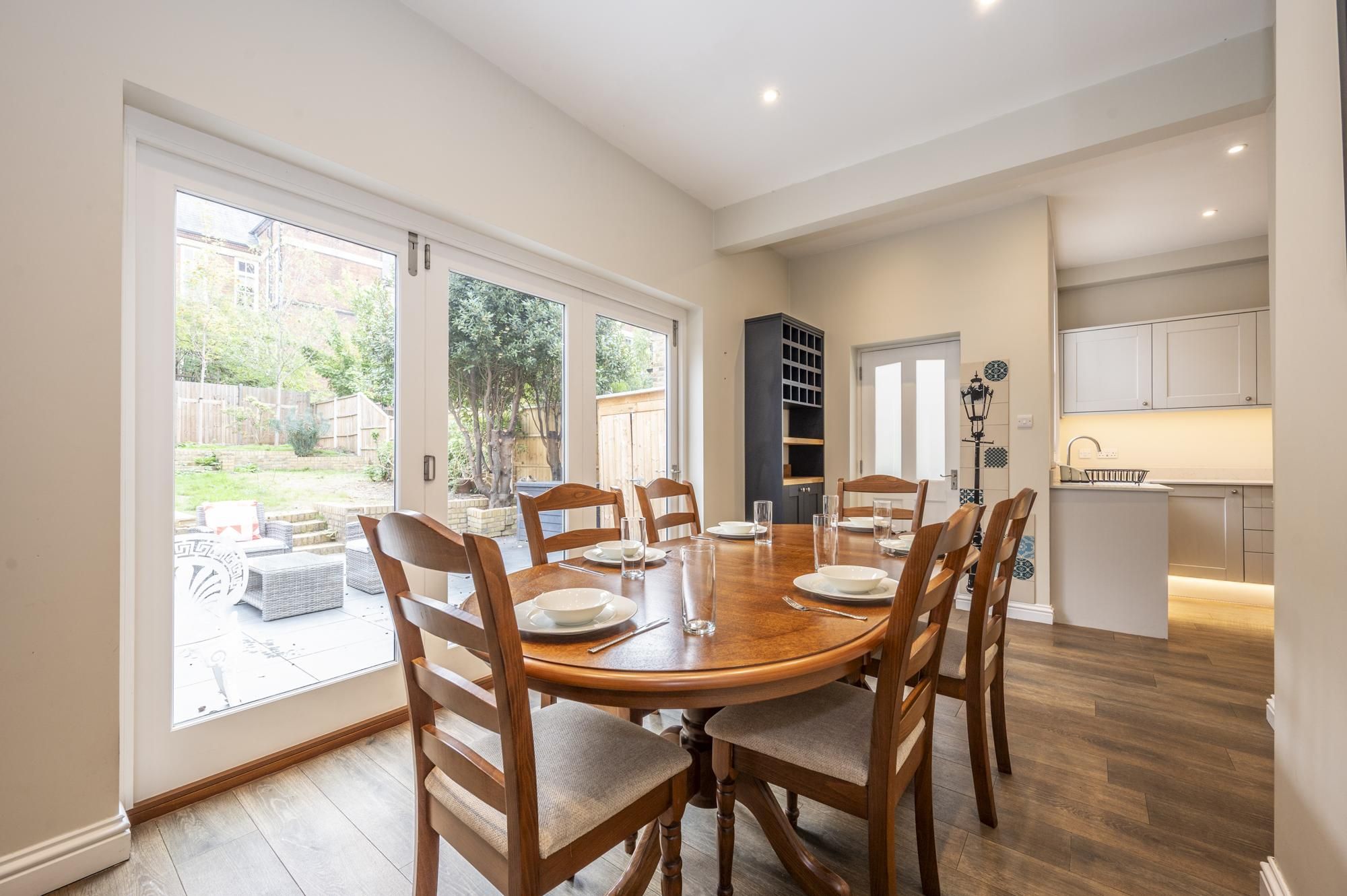 A dining area with a round wooden table, six chairs, and a view of the backyard through large windows.