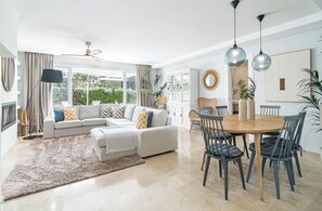 A modern living room with a sofa, ottoman, dining table, chairs, and a large window. - LVB92 - Beautiful 4-Bed Townhouse in Guadalvilla (San Pedro)
