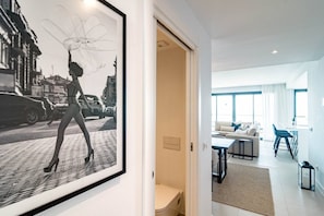 A modern interior with a framed black and white photograph on the wall, a living area with a sofa, a dining table, and a kitchen area visible through an open door. - LMe133A- Stunning flat close to beach in estepona (Estepona)
