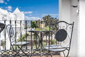 A balcony with two chairs and a small table, overlooking a street with buildings and greenery. - AP103- Aloha Pueblo Marbella by Roomservices (Marbella)