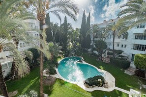 A swimming pool surrounded by palm trees and a white building with multiple windows. - Marbella apt near beach, 5 pools & gym - MR (Marbella)