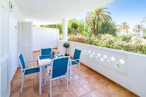 Un balcon avec une table et des chaises, un pot de fleurs et une vue sur la verdure et les palmiers.