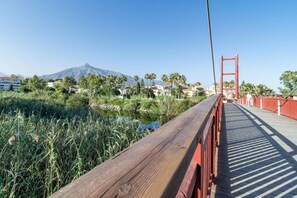 A wooden bridge with a red railing, leading to a body of water and a mountain in the background. - Beachside Apartment with Pool, Puerto Banus- PR20 (Marbella)