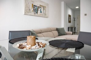 Un salon moderne avec une table basse en verre, un vase décoratif et une assiette de collations.
