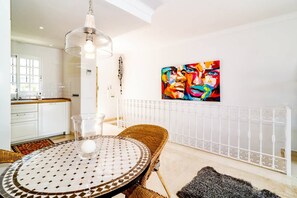 Eine moderne Küche mit weißen Schränken, ein Essbereich mit rundem Tisch und ein farbenfrohes abstraktes Gemälde an der Wand.
