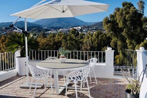 An outdoor patio with a round table and chairs, a large umbrella, and a view of a town and mountains in the background. - AP165 - Aloha Pueblo, Marbella by roomservices (Marbella)