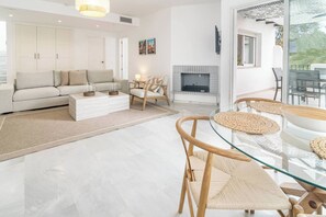 A modern living room with a sofa, coffee table, and chairs, a fireplace, and a dining area with a glass table and woven placemats. - LNm530 - Great location with private roof terrace (Marbella)