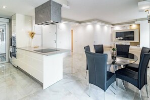 A modern kitchen with a central island, a dining area with a round table and chairs, and a built-in TV. - TErr69- Bright city gem in charming Old Town (Estepona)