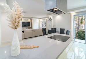 A modern kitchen with a central island, a dining area with chairs, a sofa, and a large window with a view of palm trees. - TErr69- Bright city gem in charming Old Town (Estepona)