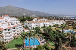 A resort with multiple white buildings, a swimming pool, and palm trees. - 2-Bed Apt with Pool, Near Puerto Banus - RG312 (Marbella)