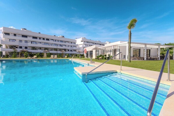 Une piscine à l’eau d’un bleu cristallin, entourée d’un bâtiment blanc doté de nombreux balcons.