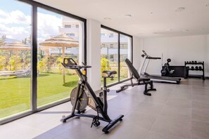 Ein modernes Fitnessstudio mit Trainingsgeräten, großen Fenstern und Blick auf einen Garten.