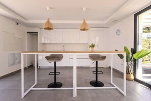 Eine moderne Küche mit weißen Schränken, einer Holz Arbeitsplatte, zwei Barhocker und Pendelleuchten.